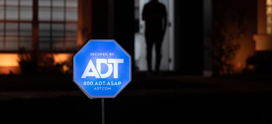 Illuminated ADT home security sign in front of a home at night.